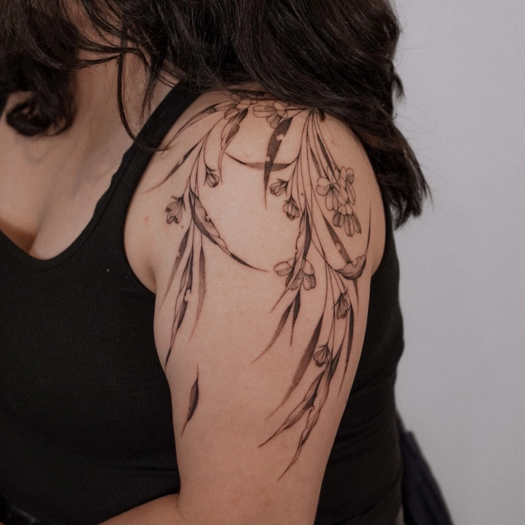 Delicate fine-line flower tattoo on shoulder and arm.