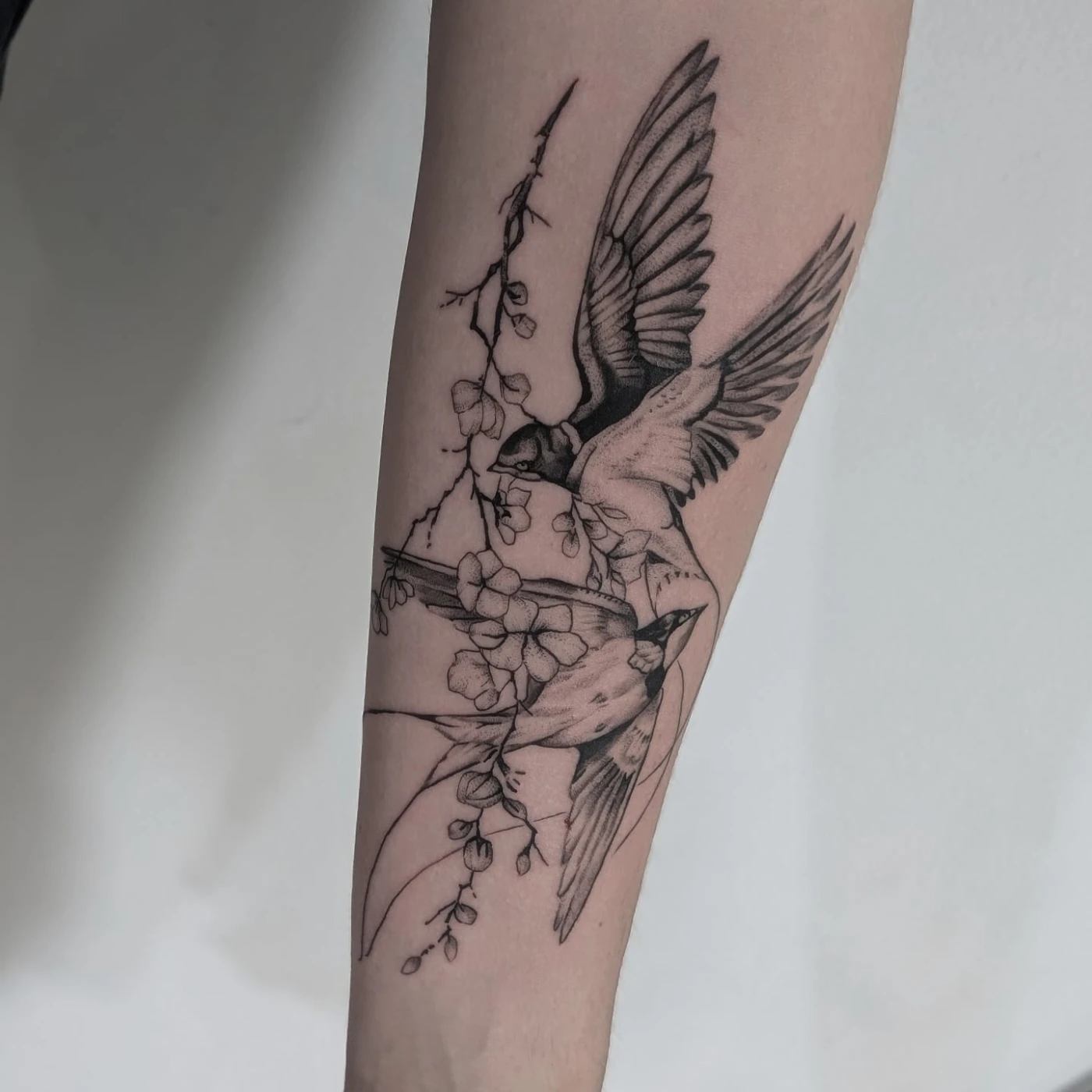 Black-and-grey birds and flowers on the forearm suited to family tribute pieces