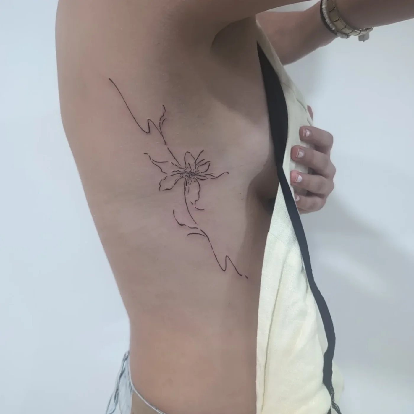 Delicate flower fine-line tattoo on rib area.