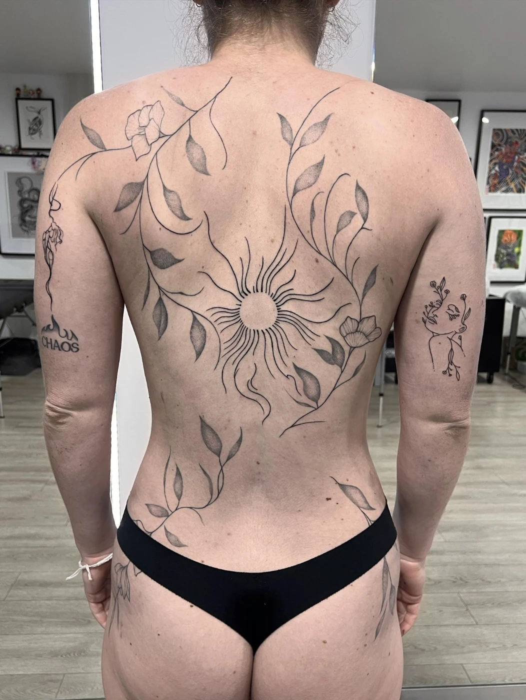Large back tattoo with sun and floral designs in fine-line style.