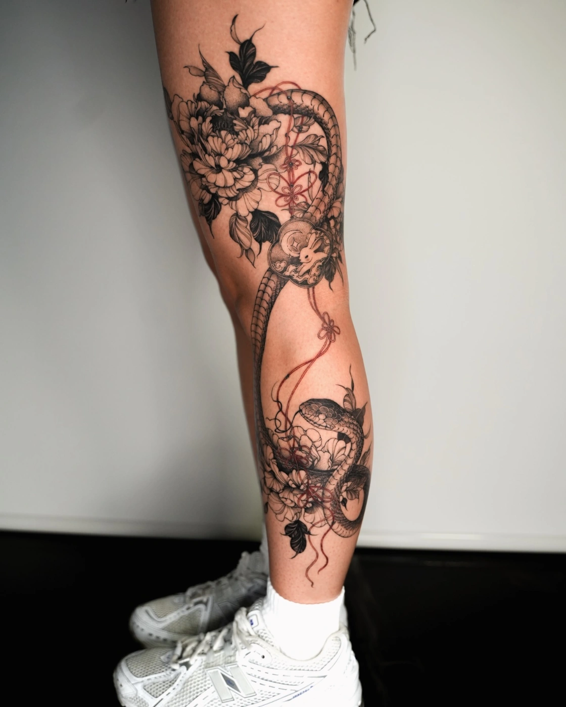 Large black-and-grey snake and lotus flower tattoo on leg.