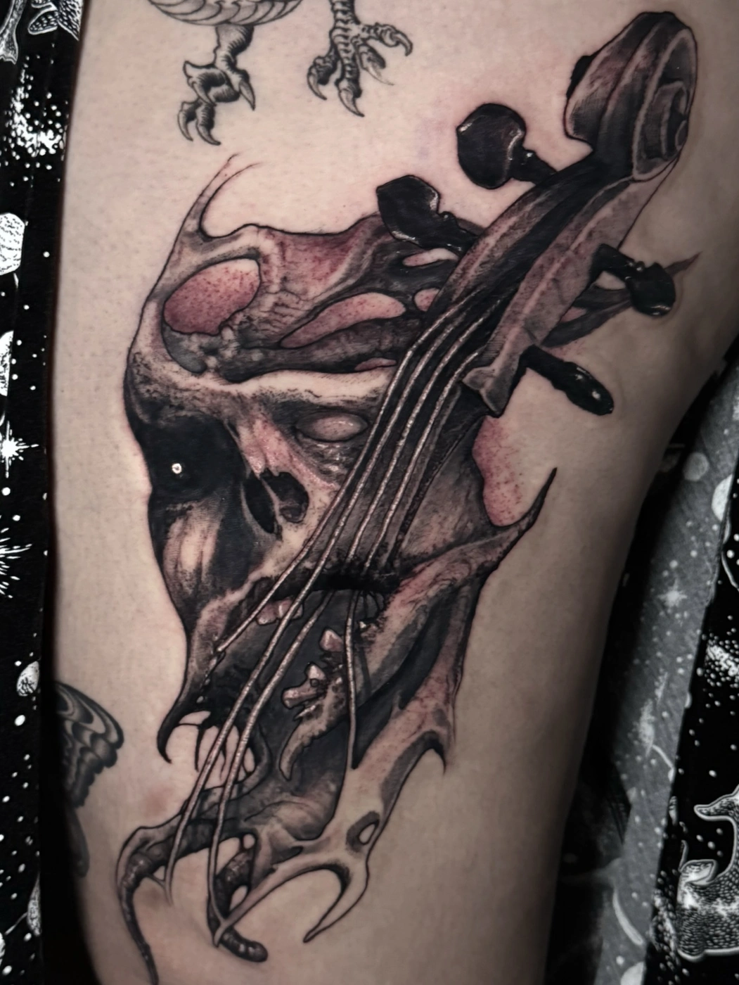 Surreal skull and violin tattoo on thigh.