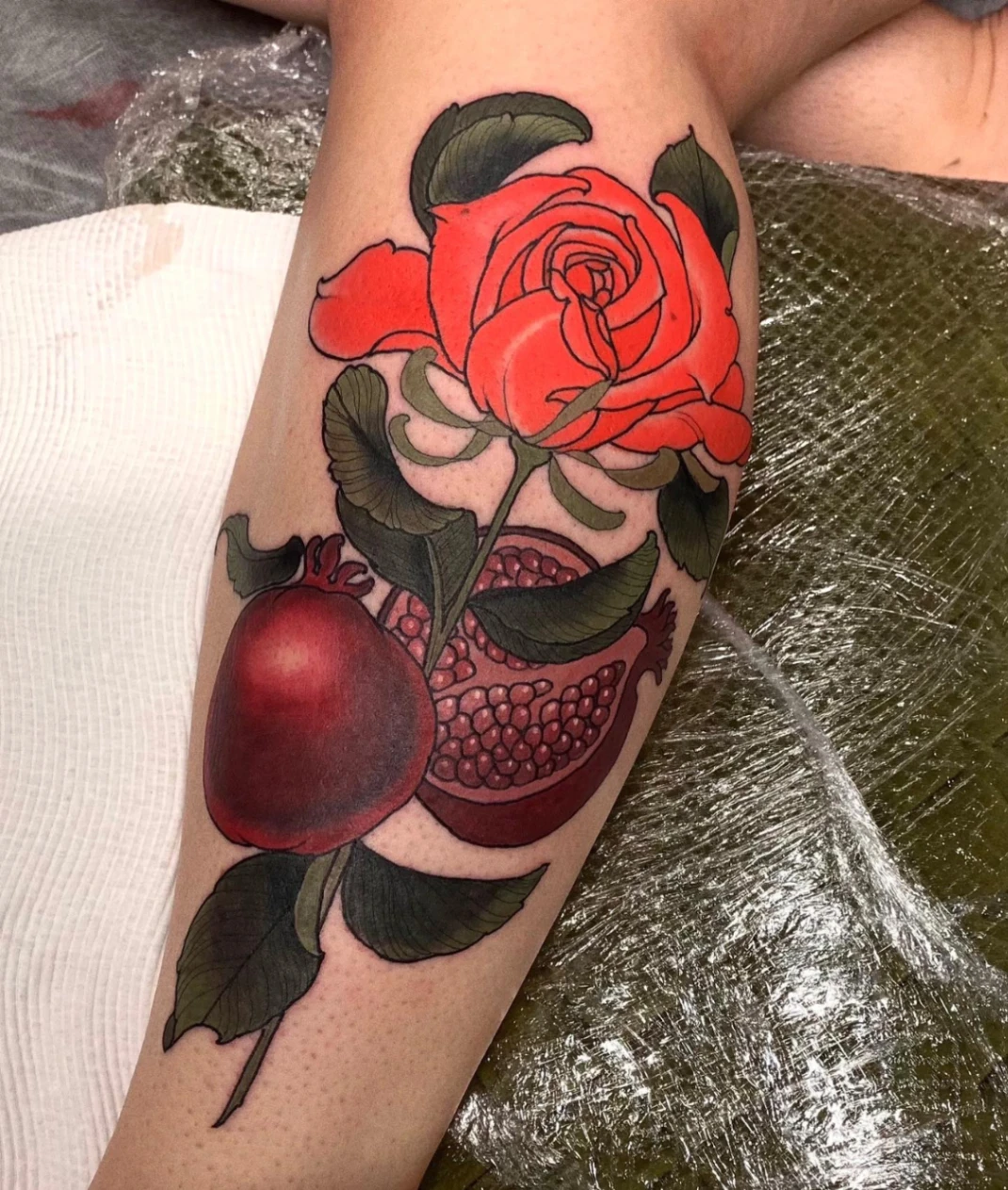 Vibrant rose and pomegranate tattoo on forearm.