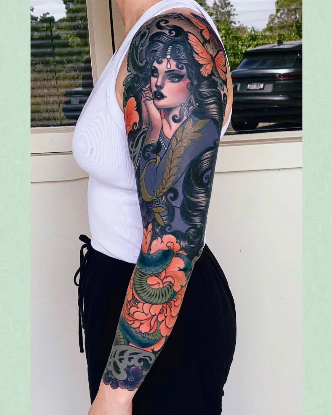 Full-sleeve tattoo of a woman with flowers and a snake.