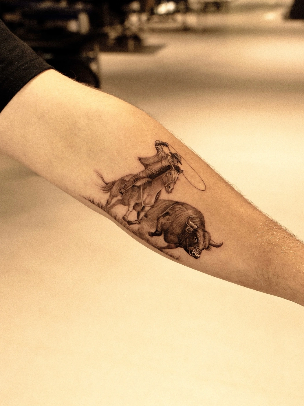 Realism tattoo of a cowboy roping a bull on forearm.