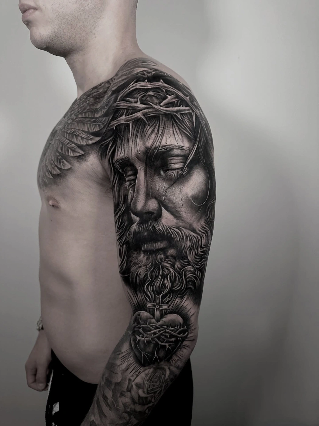 Realistic black-and-grey tattoo of Jesus on full sleeve.