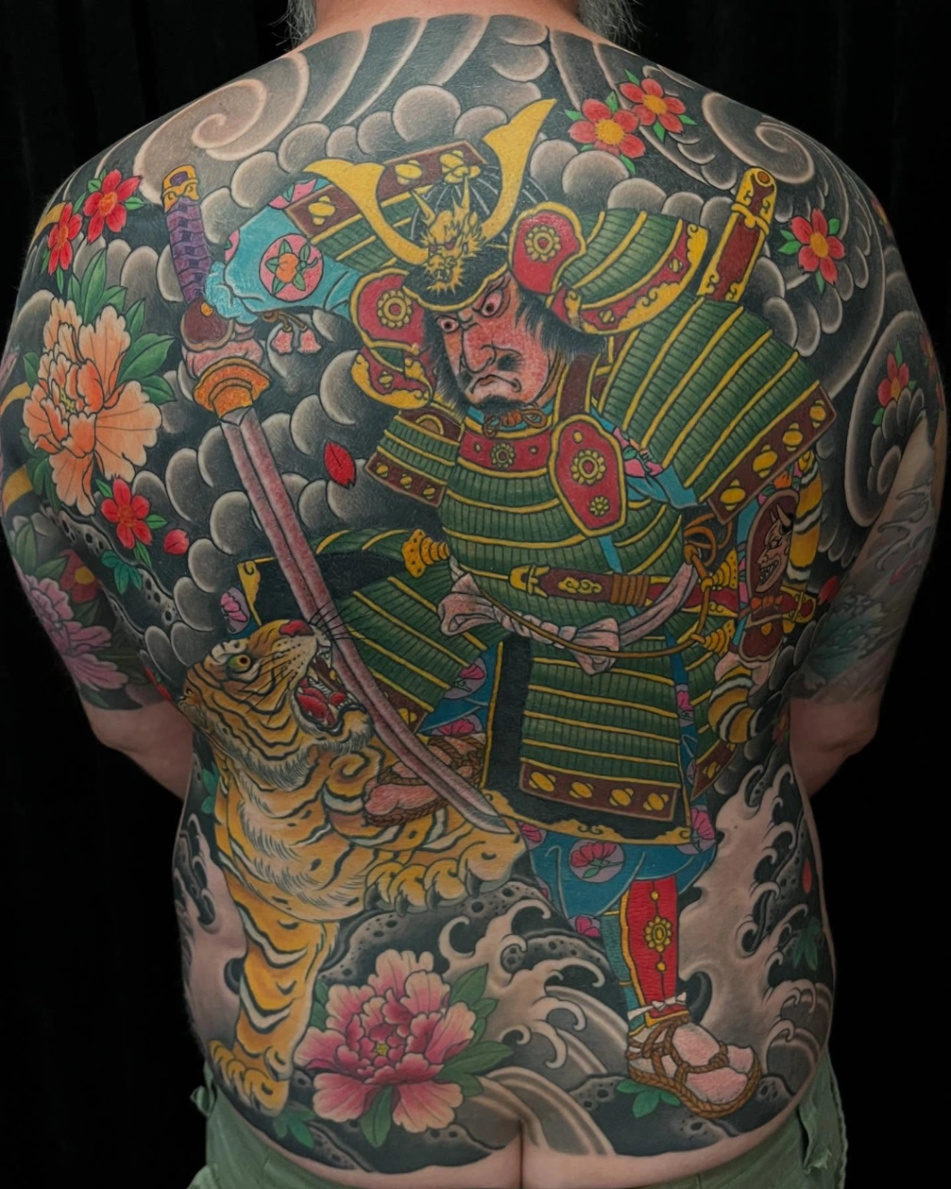 Large back tattoo of a samurai and tiger in vibrant colors.