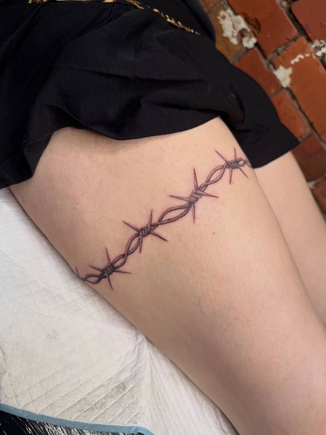 Minimalist barbed wire tattoo on thigh.
