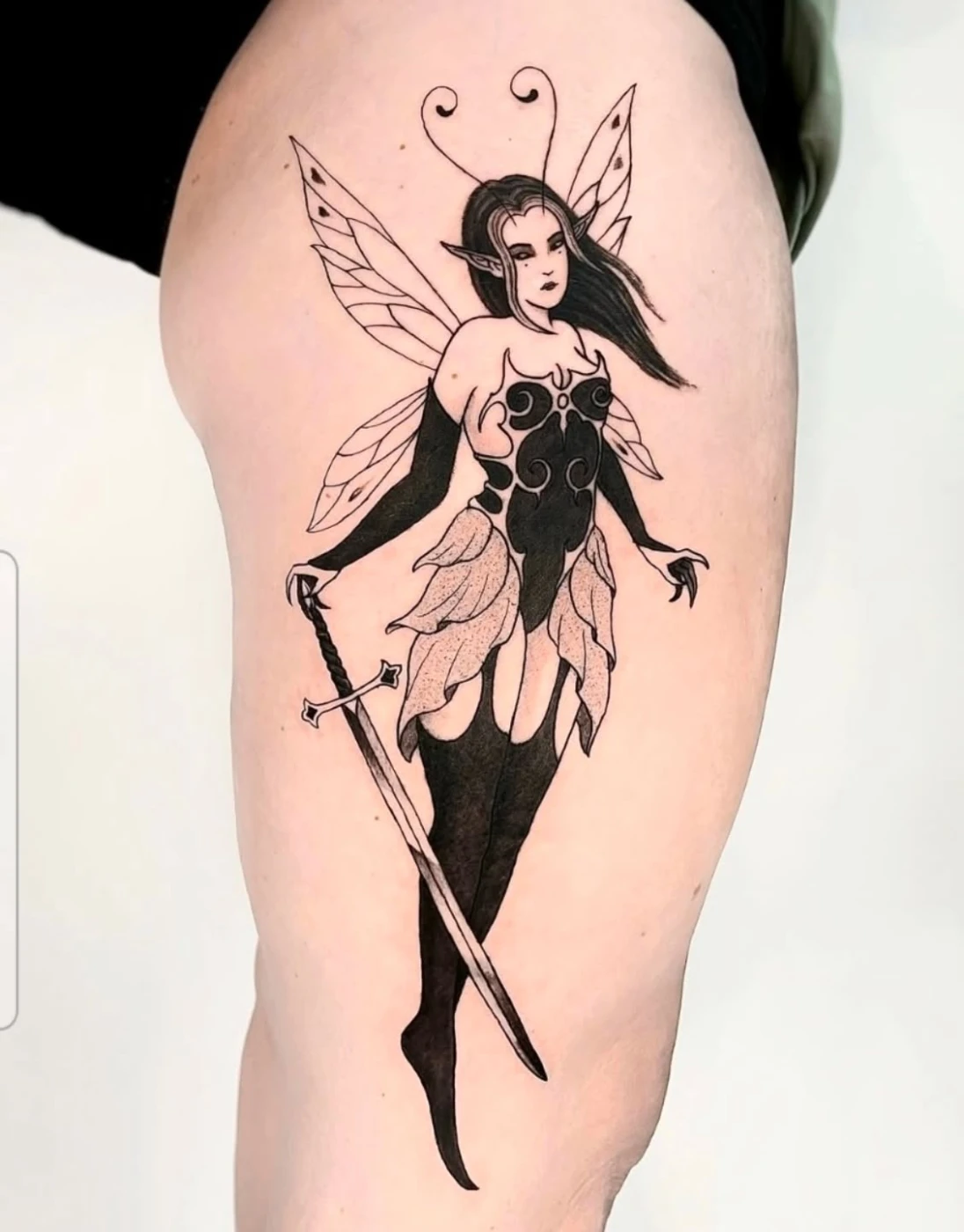 Illustrative fairy tattoo with wings and sword on thigh.