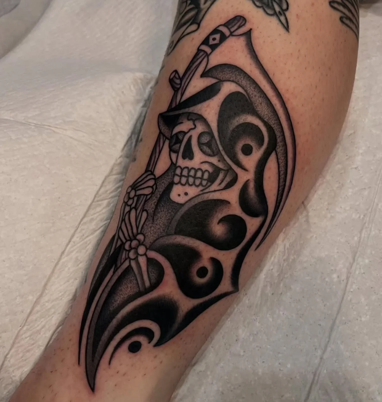 Detailed blackwork skull and grim reaper tattoo on calf.