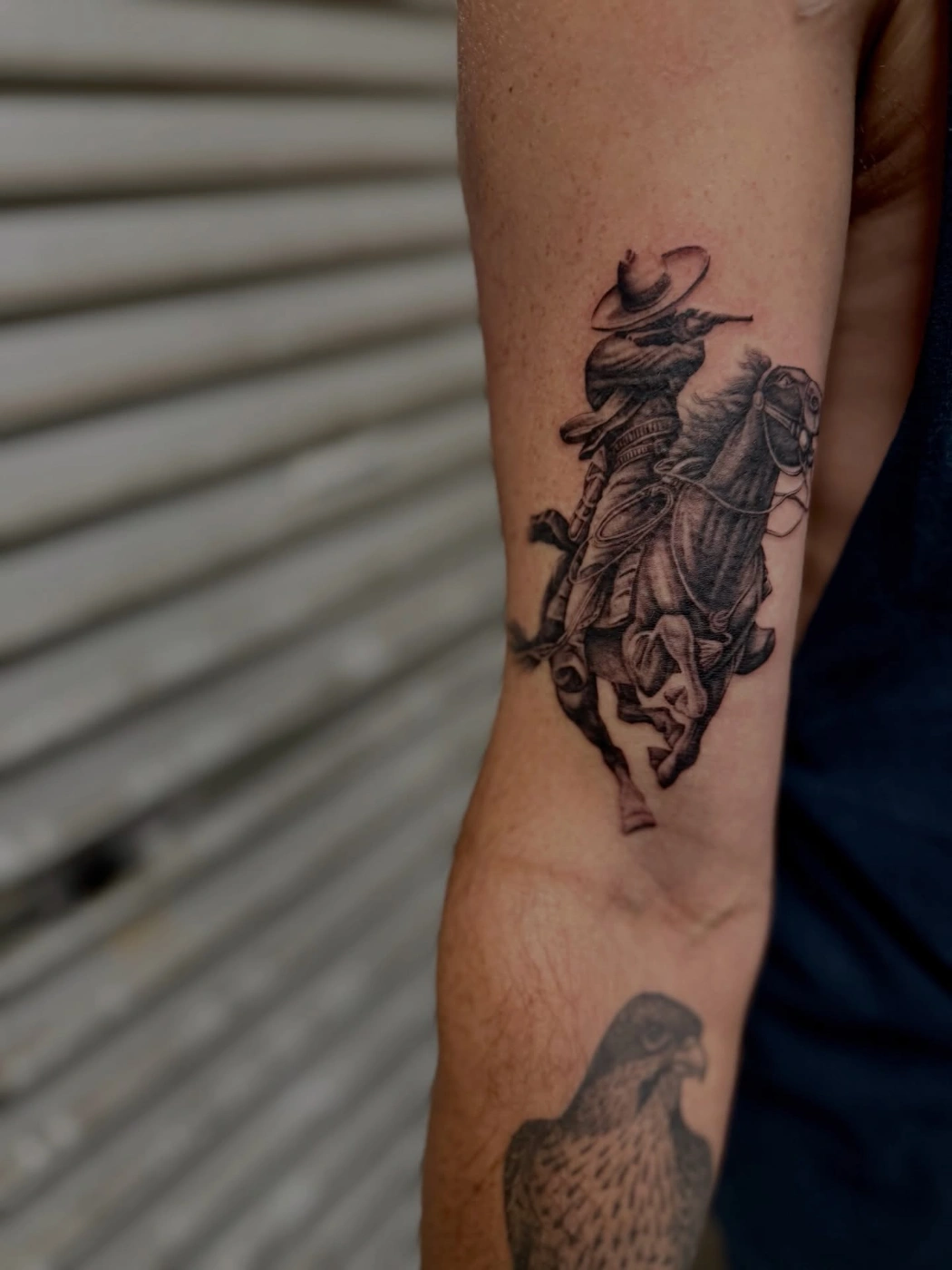 Black-and-grey cowboy riding a horse tattoo on arm.