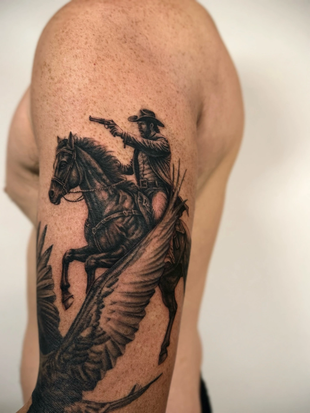 Realistic cowboy riding a winged horse tattoo on bicep.