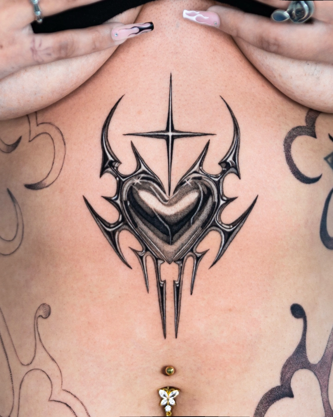 Black-and-grey heart tattoo with tribal elements on chest.