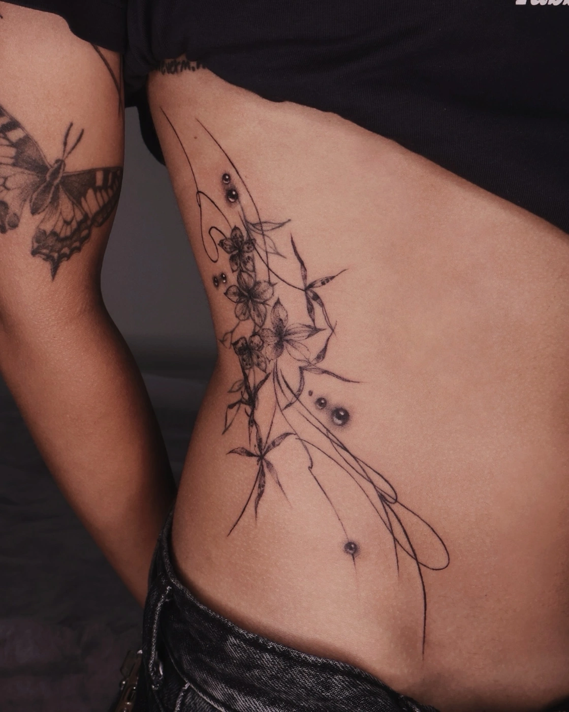 Delicate fine-line flower tattoo on the rib side.