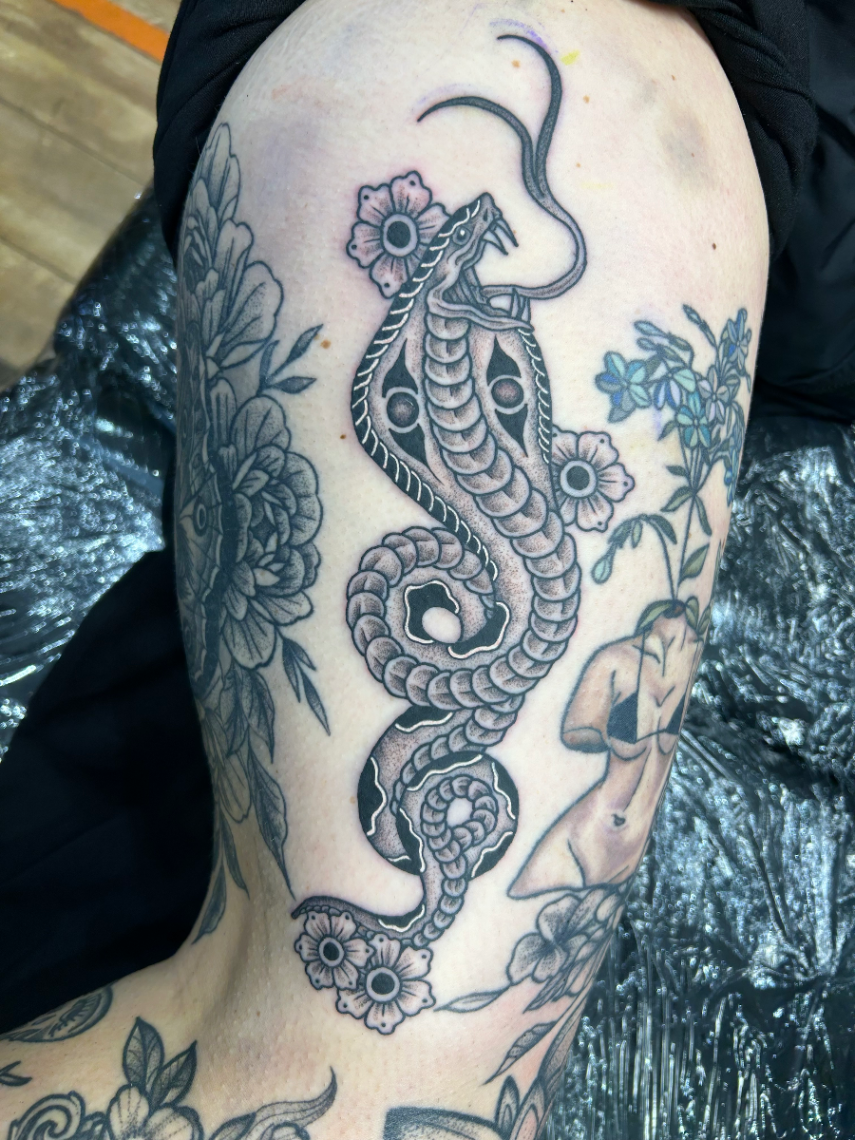 Detailed black-and-grey snake tattoo with flowers on the arm.