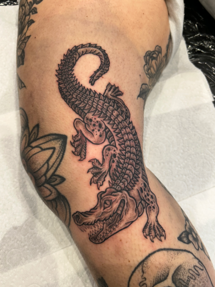 Illustrative alligator tattoo on forearm in blackwork style.