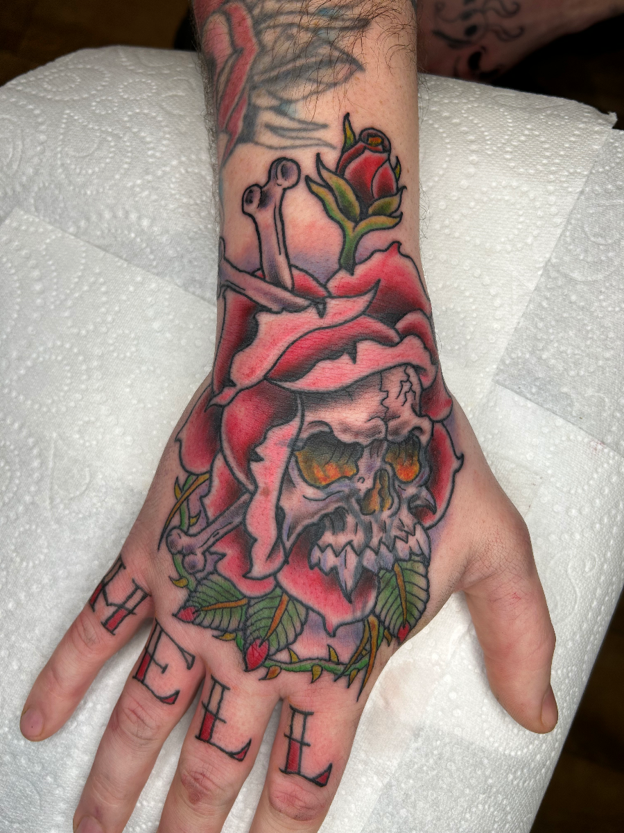 Colorful skull and rose tattoo on a hand.