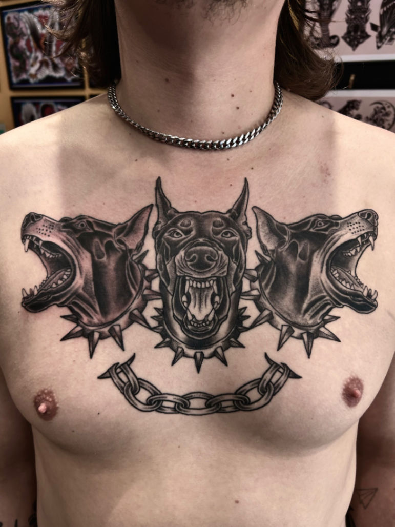 Black-and-grey tattoo of three dog heads on chest.