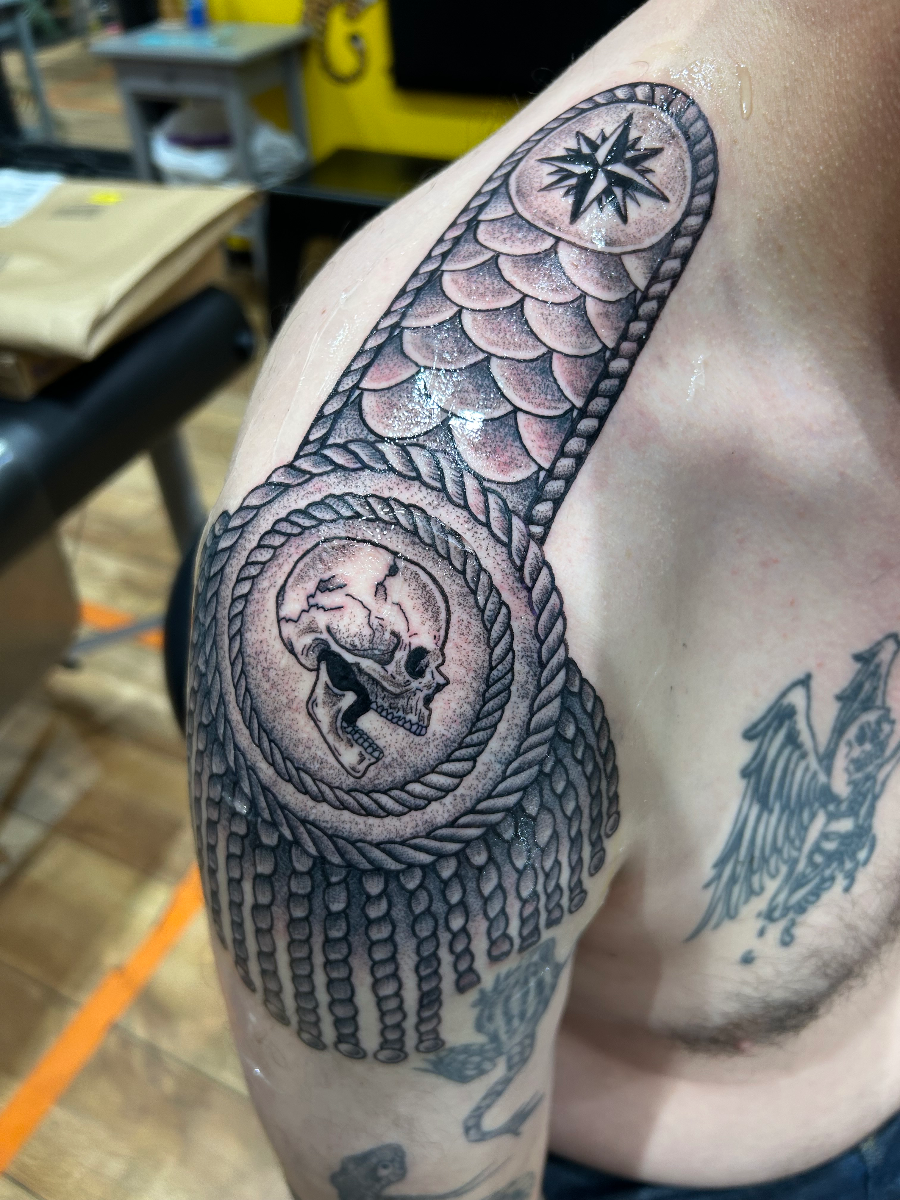 Black-and-grey skull tattoo on shoulder with rope and compass.