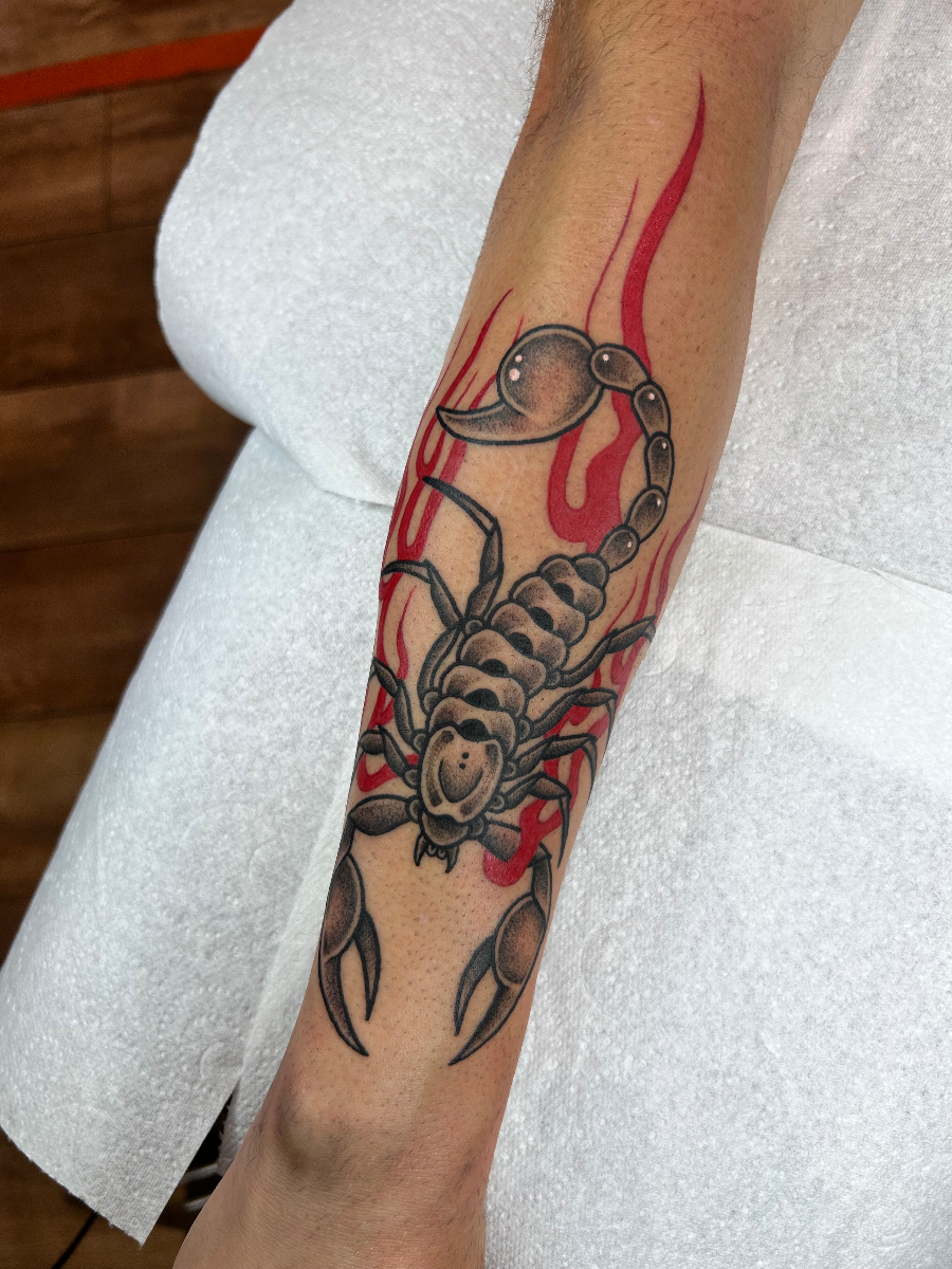 Medium scorpion tattoo with red flames on forearm.