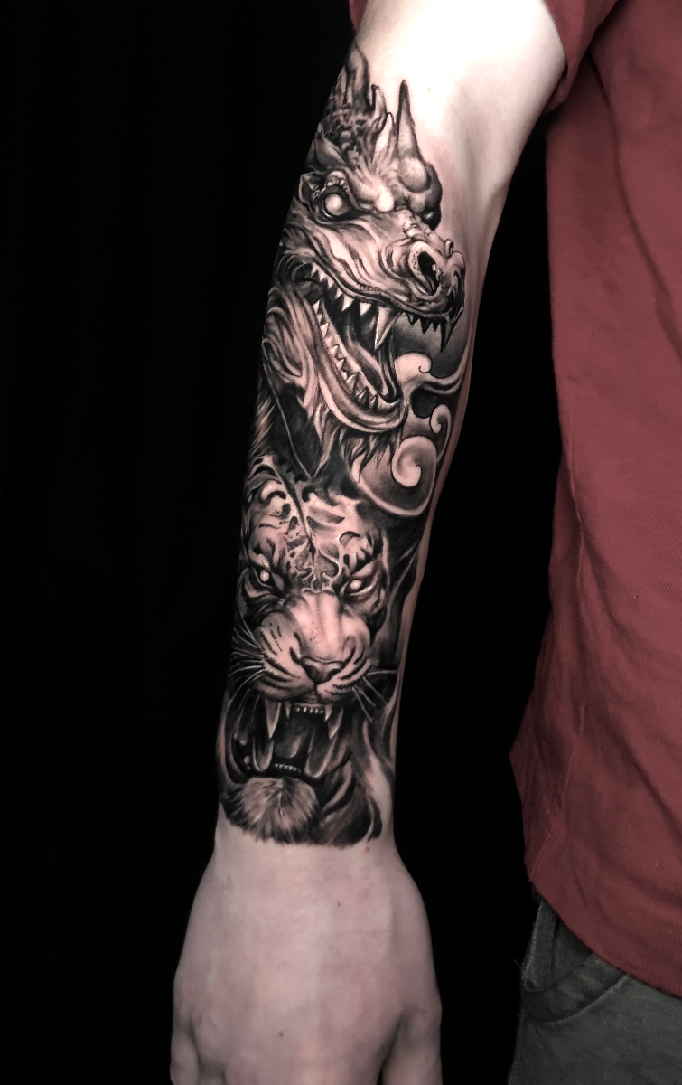 Black and grey tattoo of a dragon and tiger on forearm.