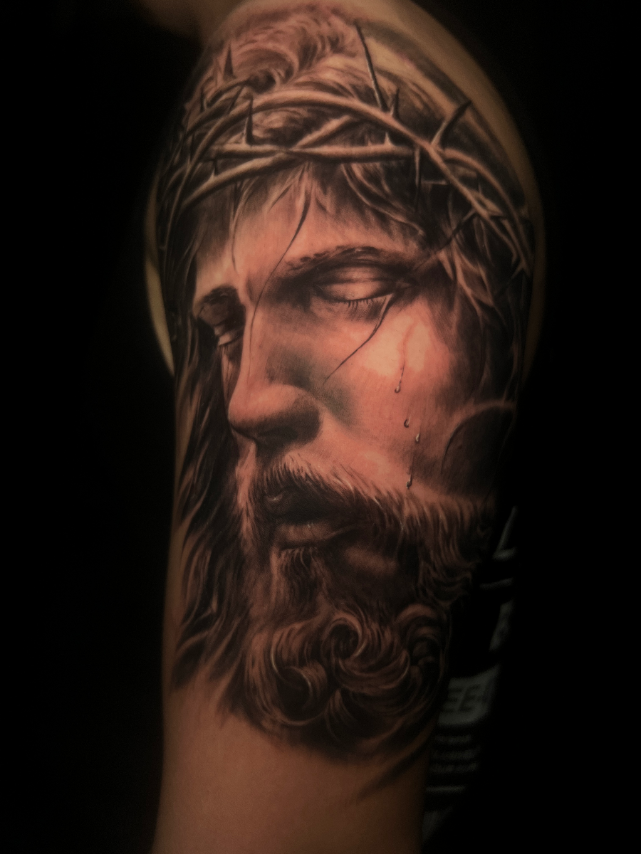 Realistic black-and-grey tattoo of Jesus with crown of thorns.
