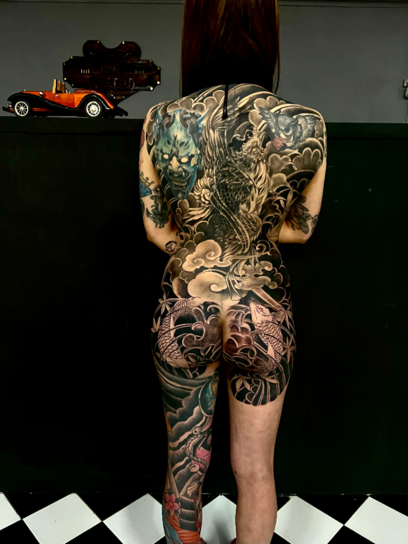 Large black and grey tattoo of a dragon and koi fish on back and thigh.