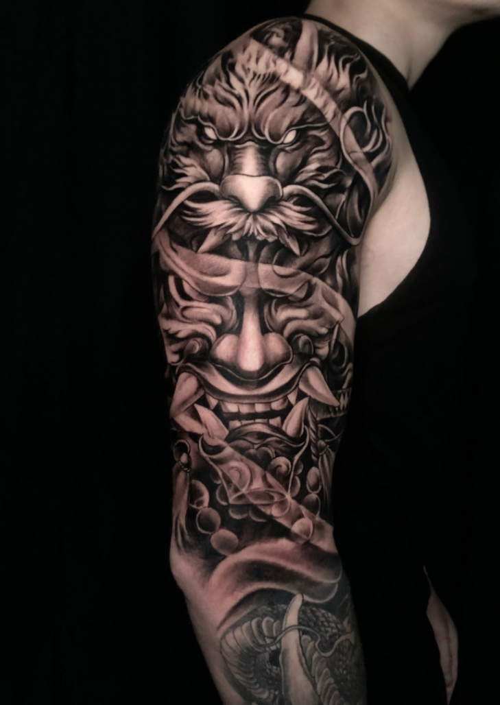 Detailed black-and-grey full-sleeve tattoo of a lion and mask.