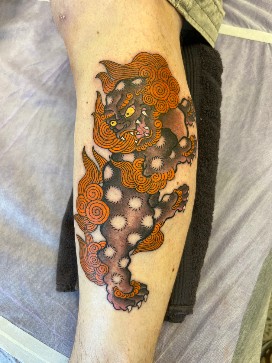 Japanese lion-dog tattoo on leg with clouds and flames.
