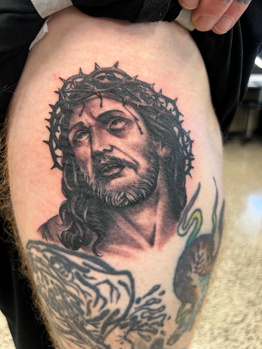 Realistic black-and-grey tattoo of Jesus on thigh.