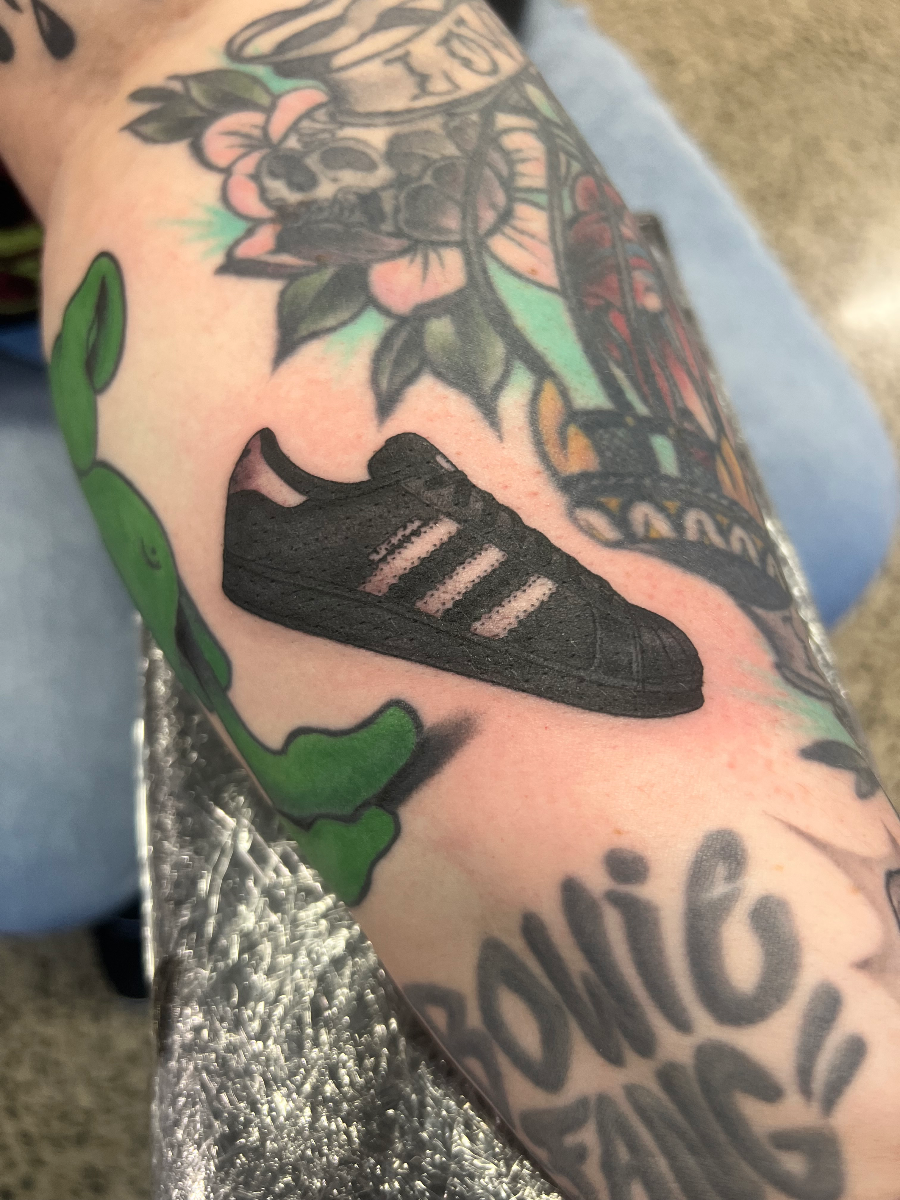Colorful Adidas shoe tattoo on forearm with alien and flowers.