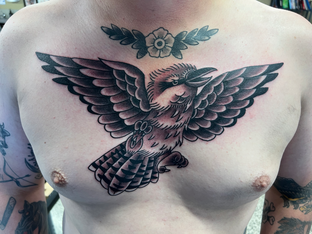 Traditional black-and-grey bird tattoo on chest with floral design.