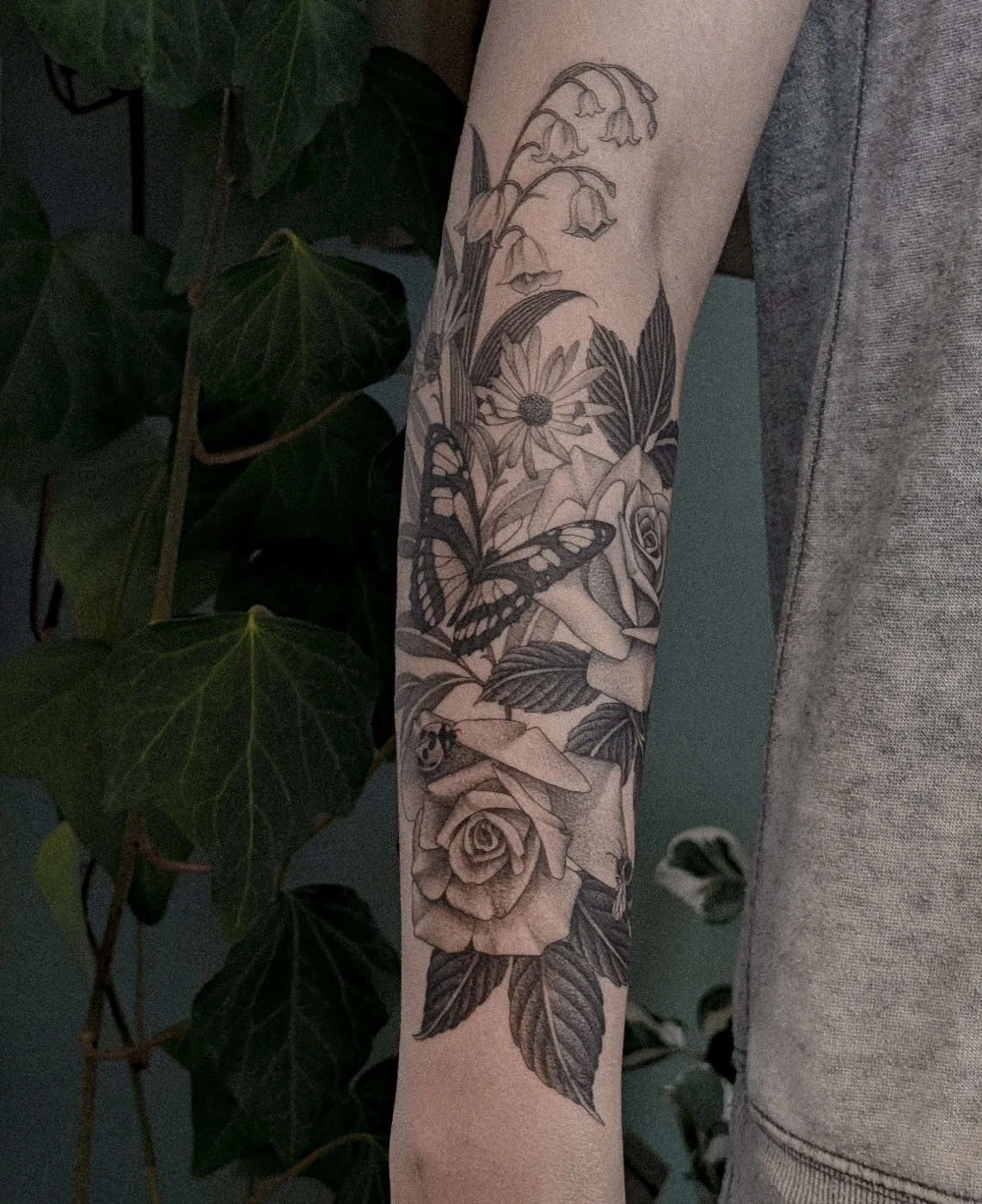 Black-and-grey tattoo of a butterfly and roses on forearm.