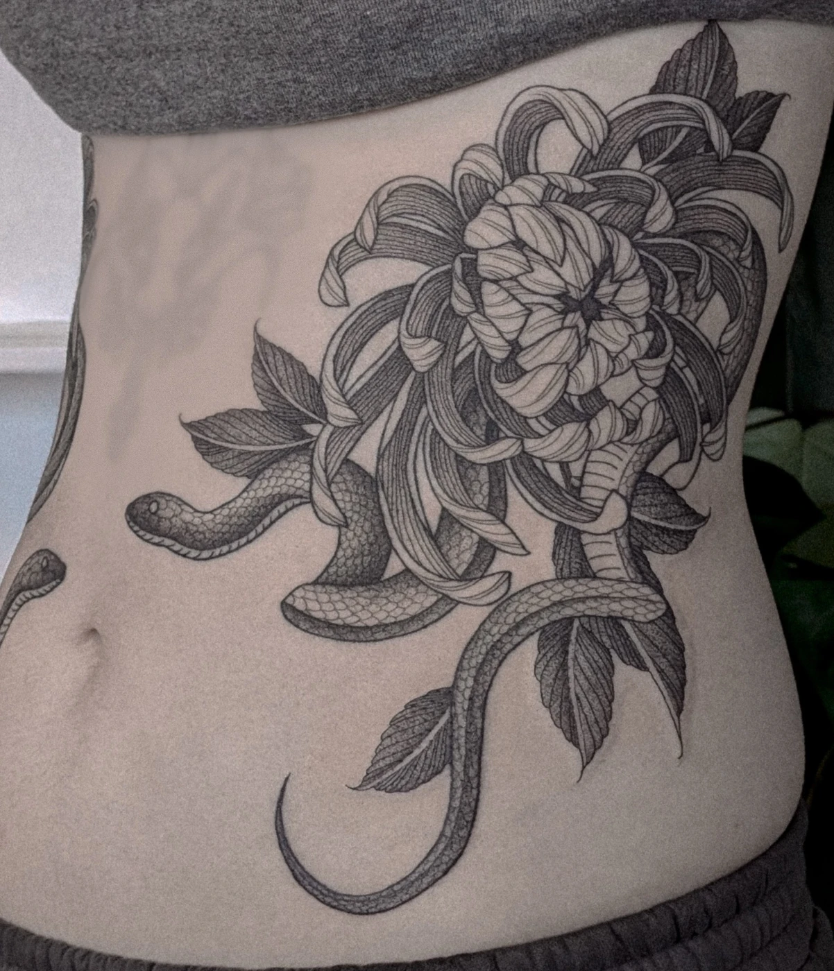 Large black-and-grey snake and flower tattoo on rib.
