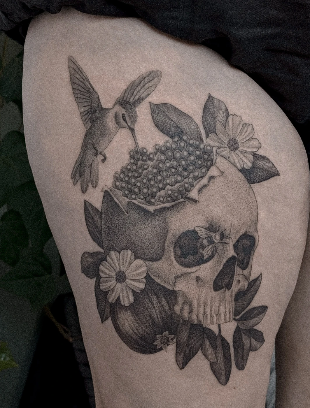 Black and grey tattoo of a skull with a hummingbird and flowers.