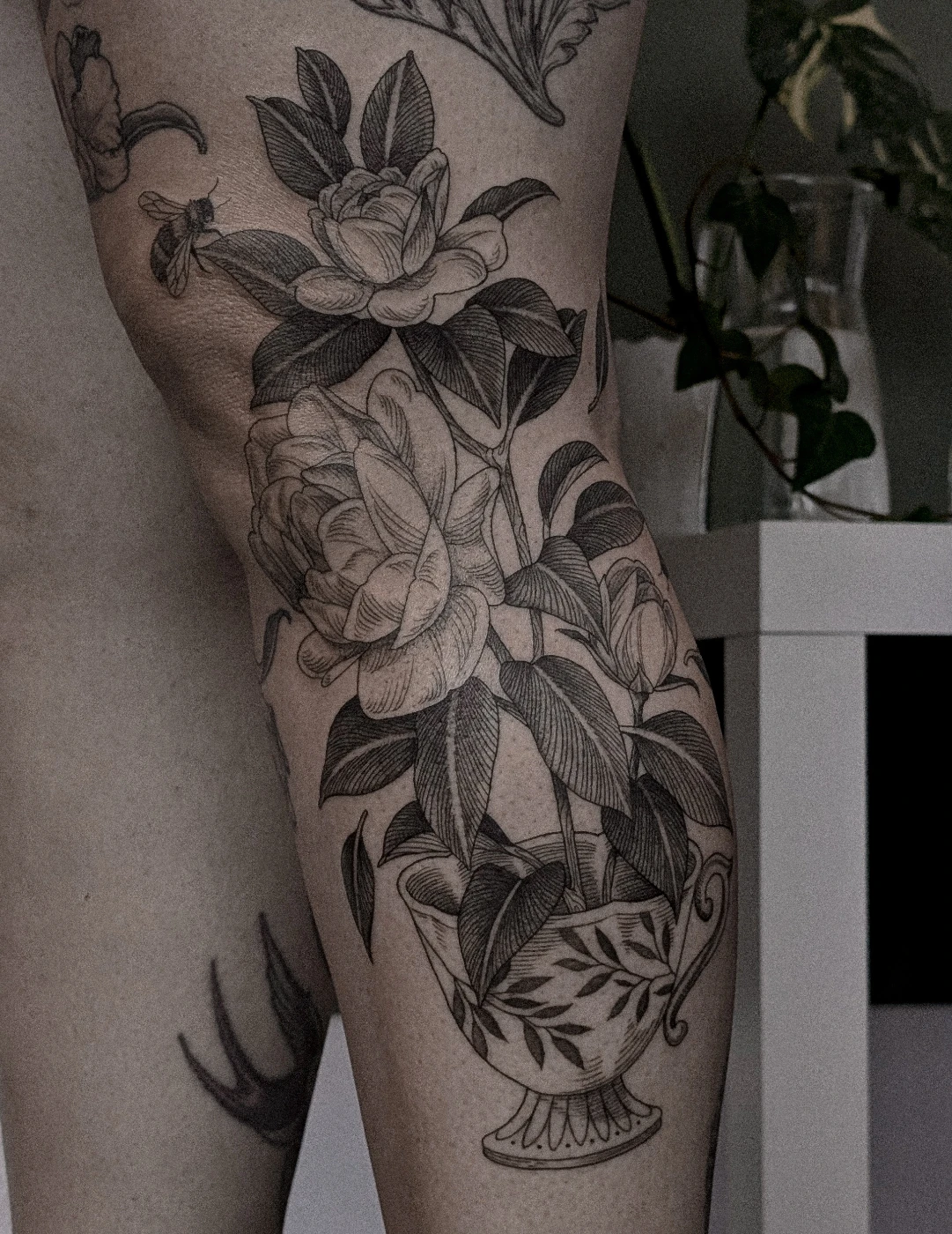 Black-and-grey floral tattoo on thigh in a vase.
