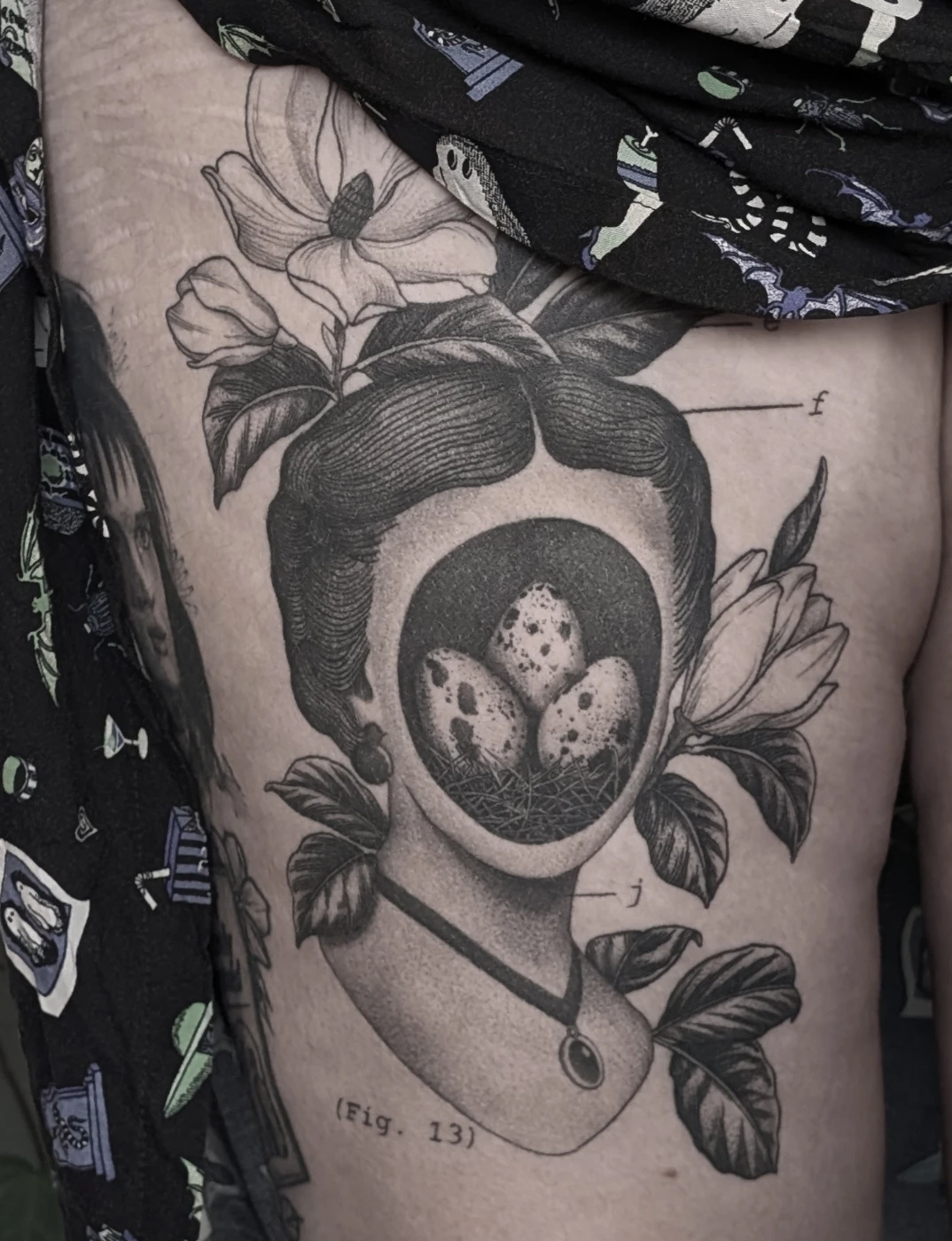 Black-and-grey illustrative tattoo of a woman with flowers and eggs.
