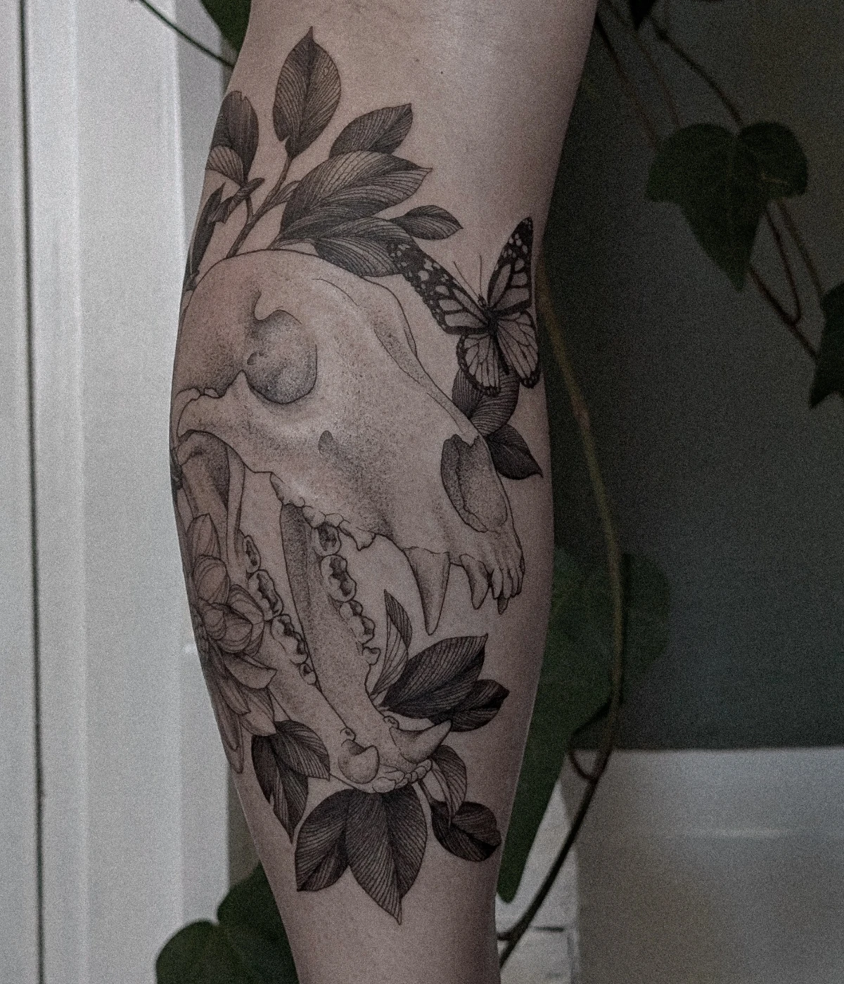 Black-and-grey skull tattoo with flowers and butterfly on calf.