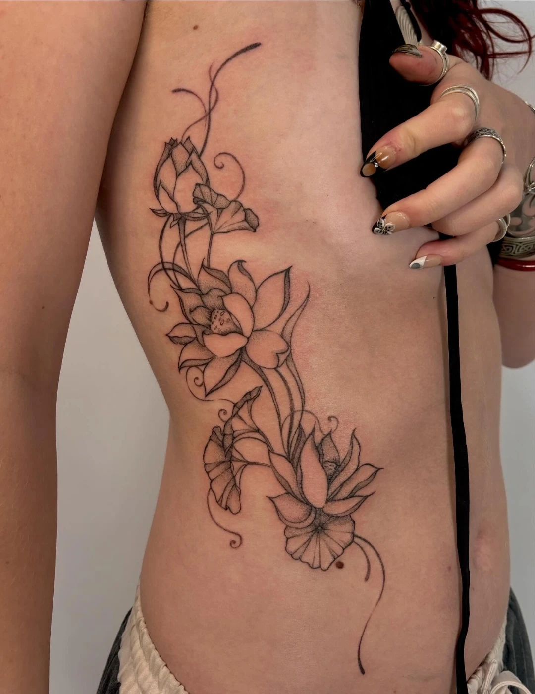 Elegant black-and-grey fine-line lotus flower tattoo on rib.