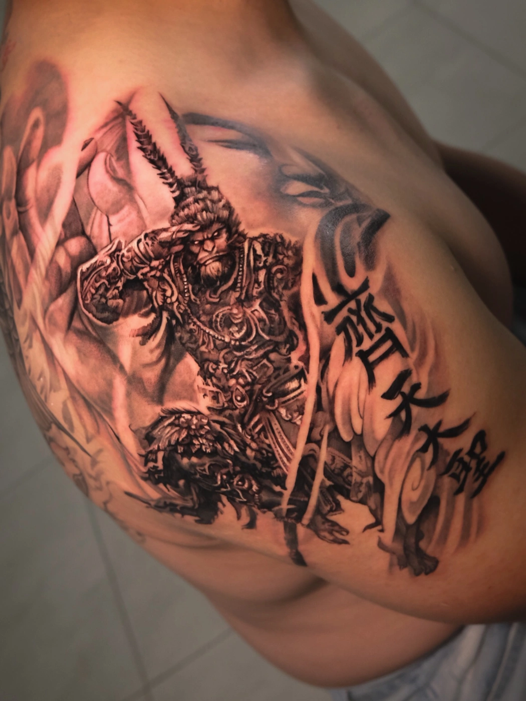 Black-and-grey tattoo of a warrior on shoulder and arm.