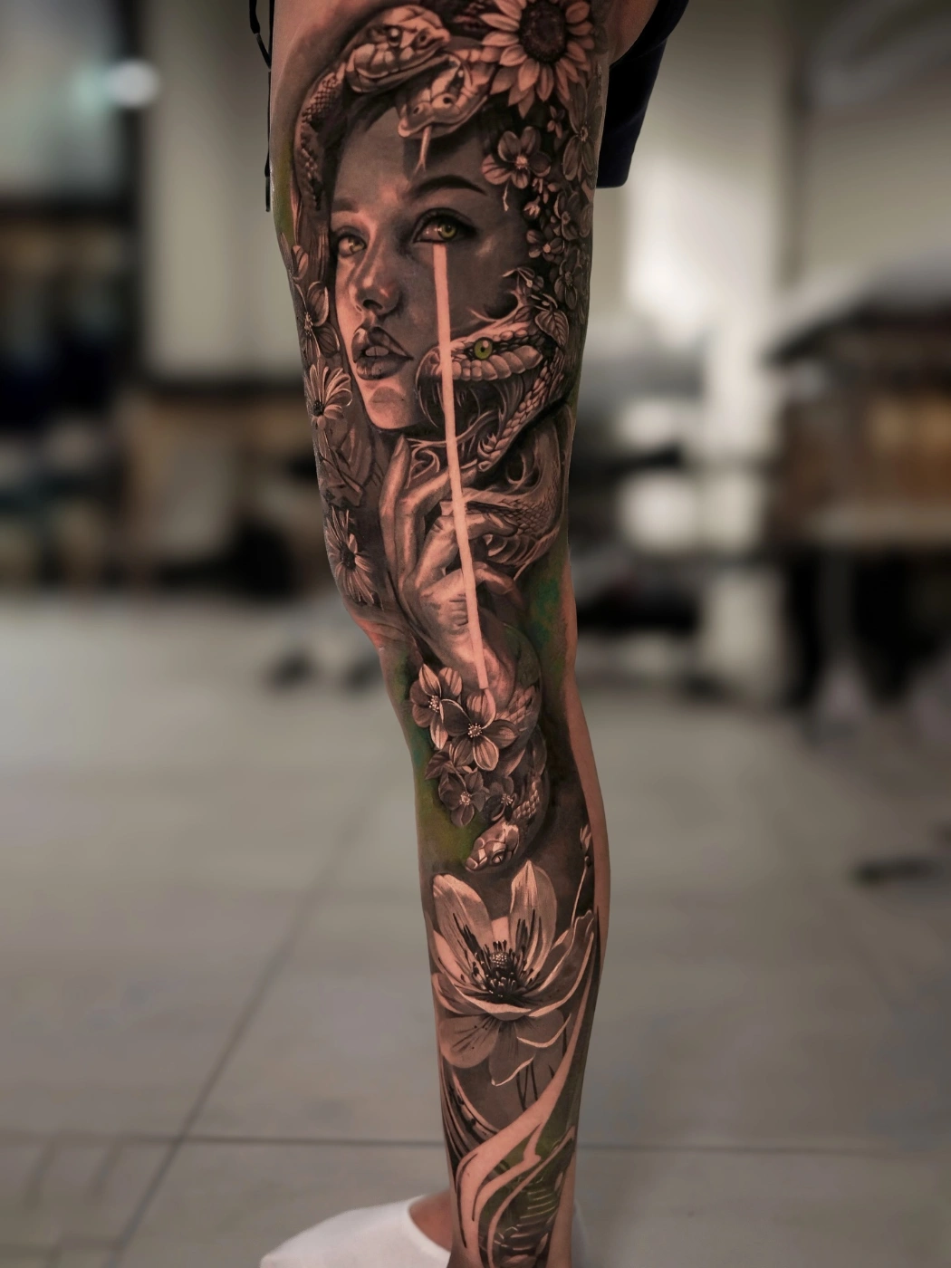 Realistic black and grey tattoo of a woman with a snake and flowers.