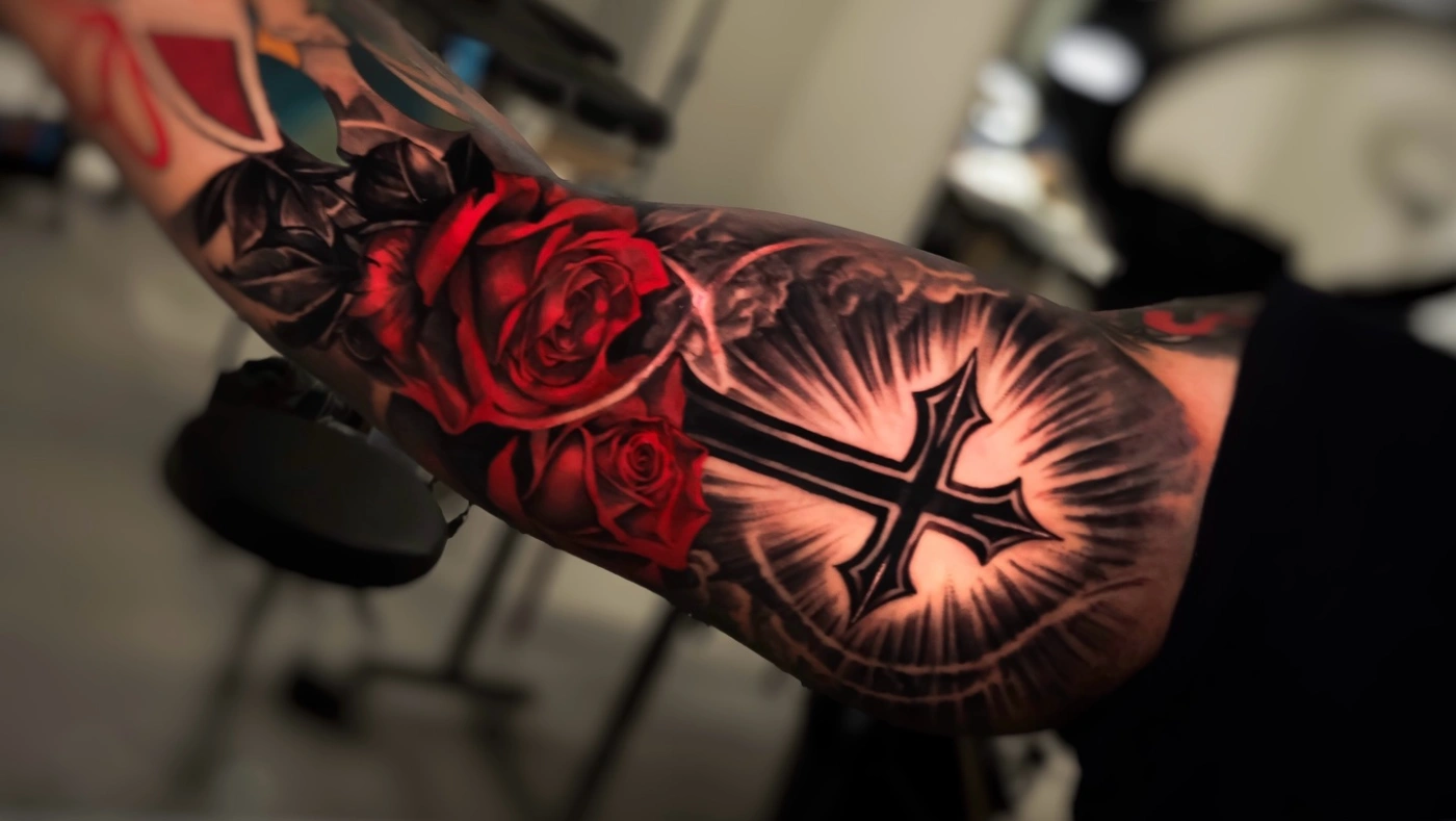 Large arm tattoo of roses and a cross with light rays.