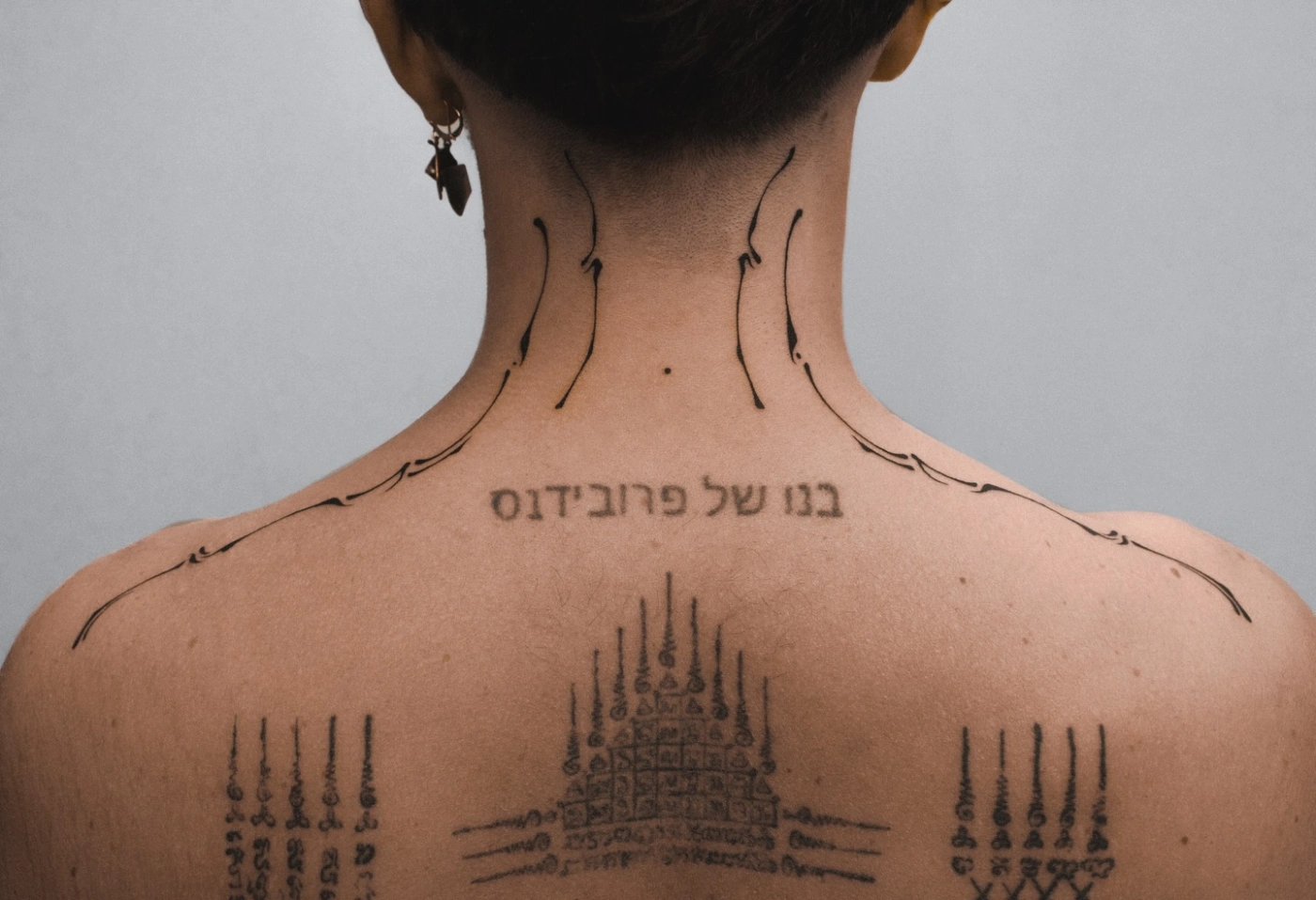 Large blackwork tattoo on the back featuring geometric shapes and script.