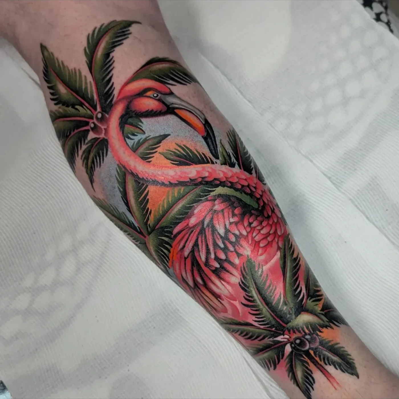 Colorful flamingo tattoo on forearm with tropical leaves.