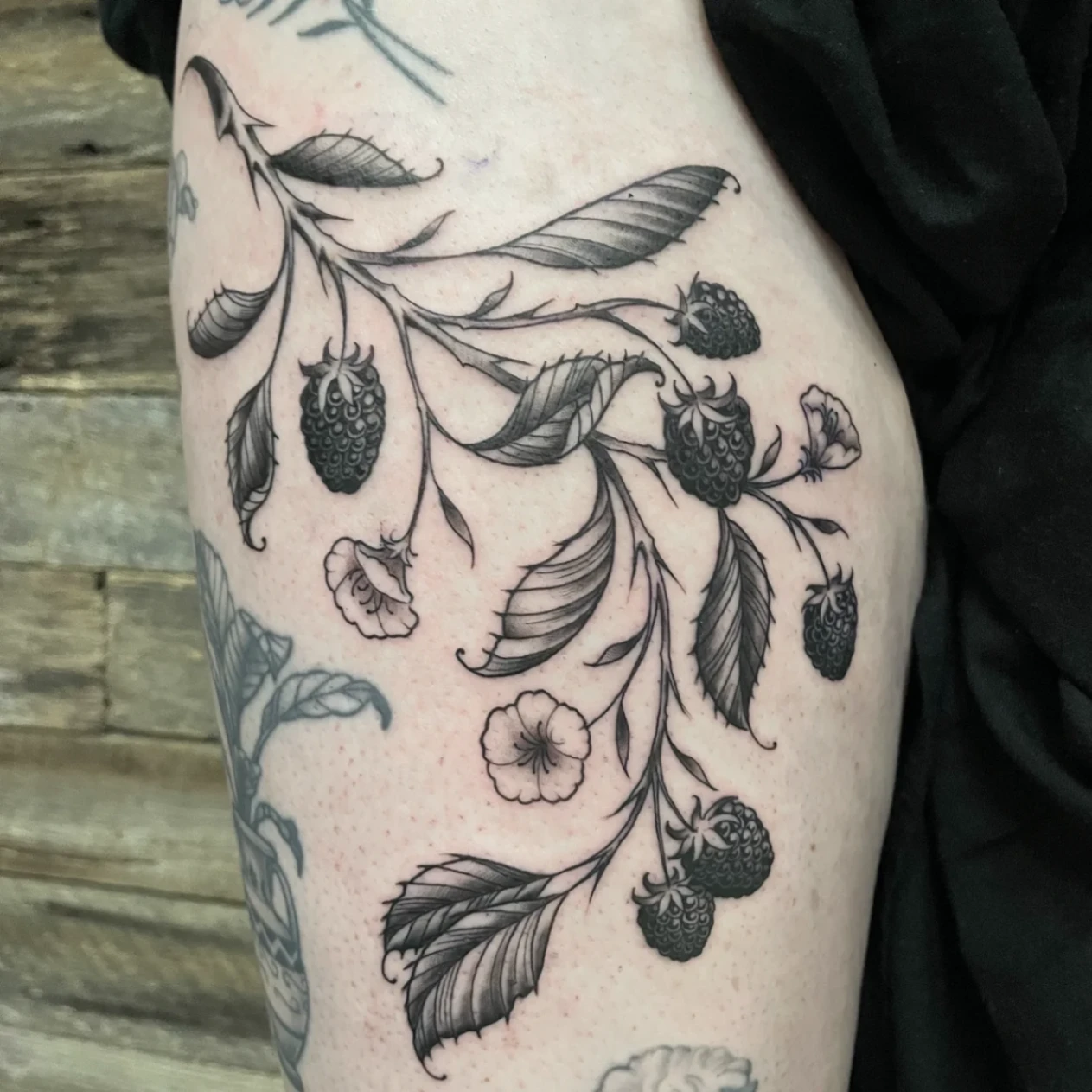 Black-and-grey floral tattoo on the arm featuring berries and leaves.
