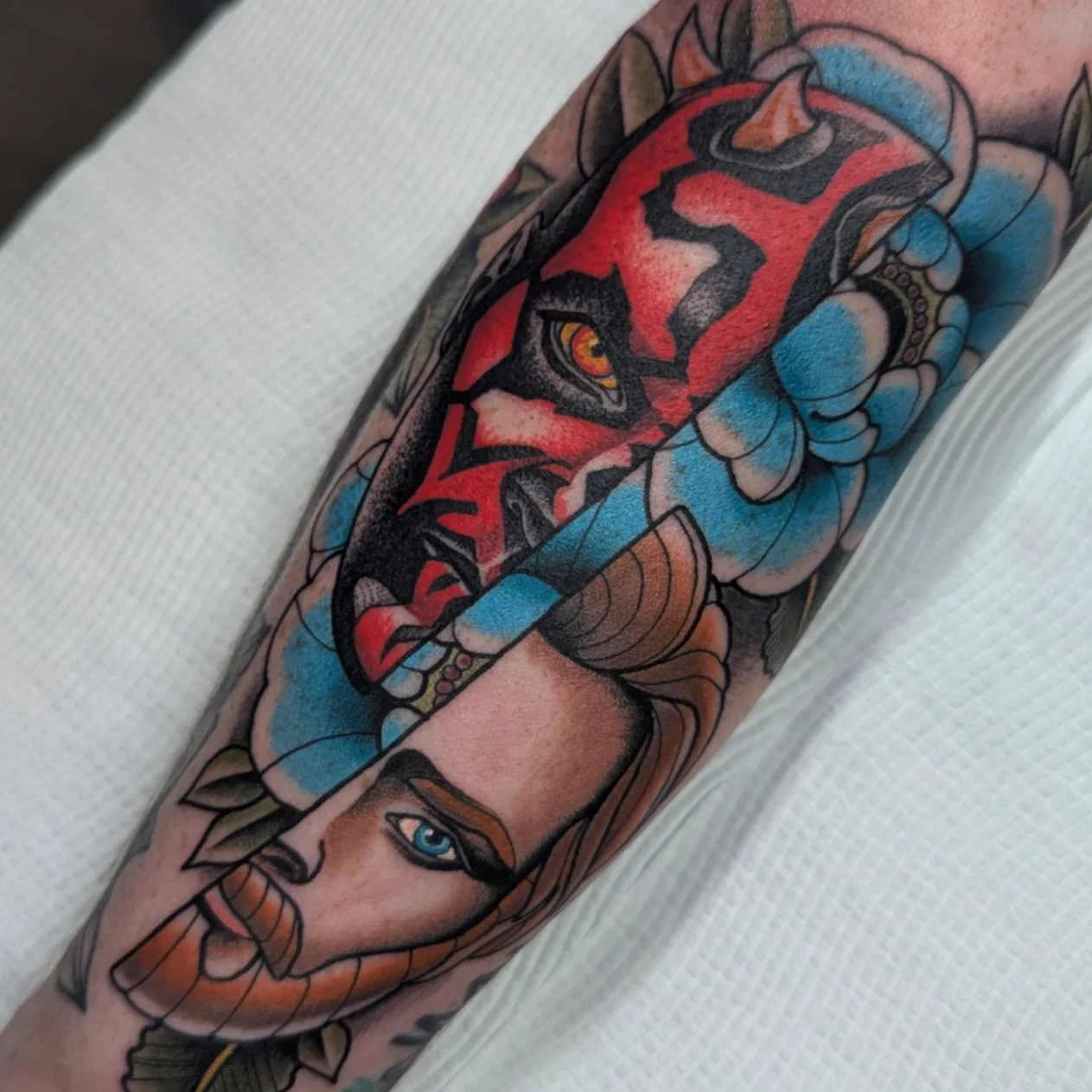 Colorful illustrative tattoo on forearm featuring mythical figures.