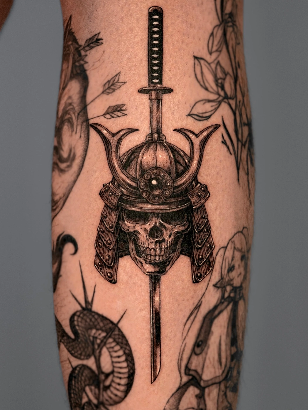 Detailed skull with samurai helmet and sword tattoo on forearm.