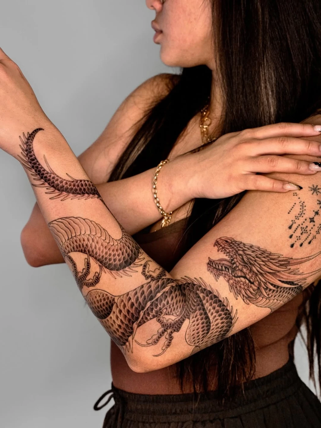 Large black-and-grey dragon tattoo on a woman's arm.