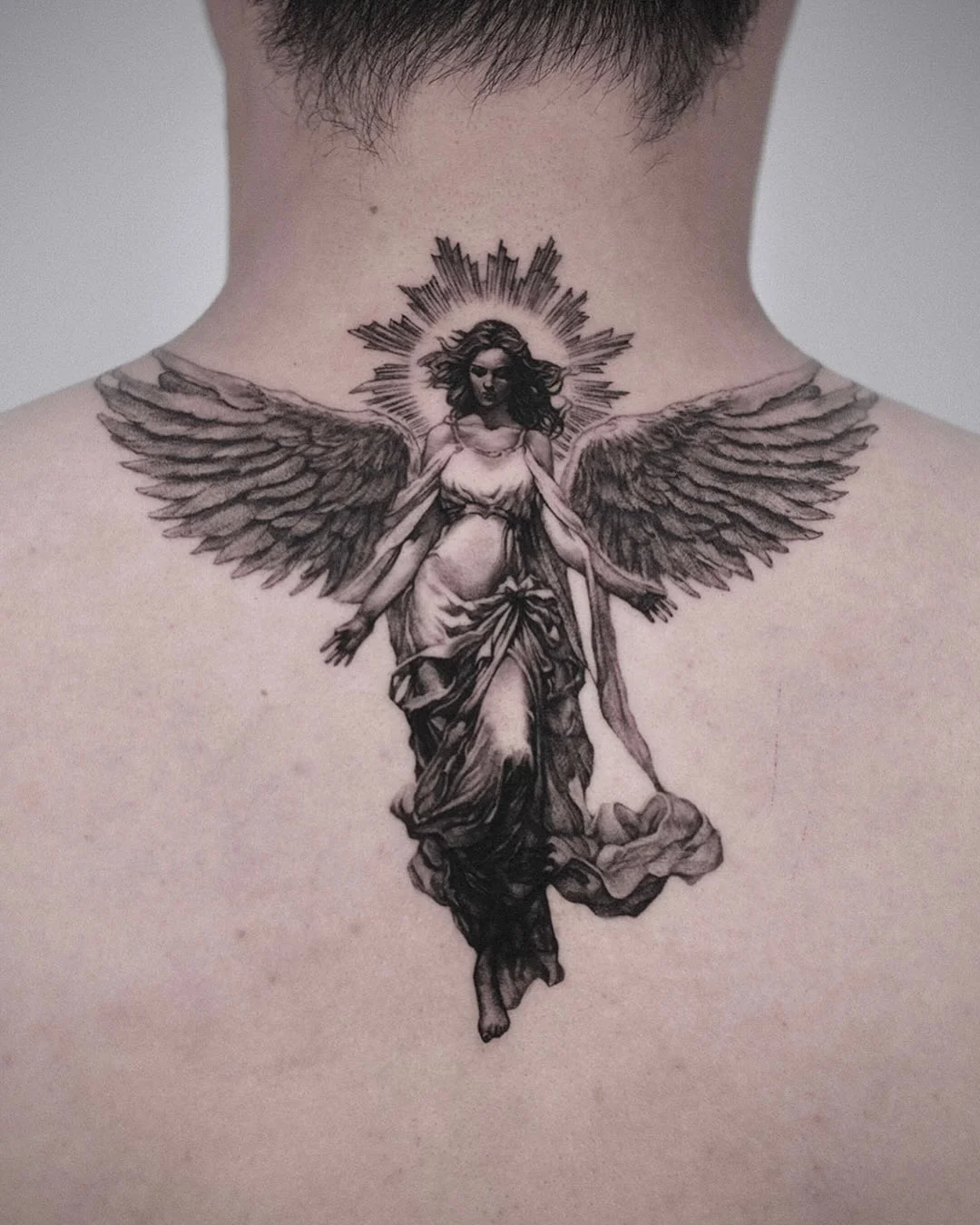 Detailed black-and-grey angel tattoo on the back.