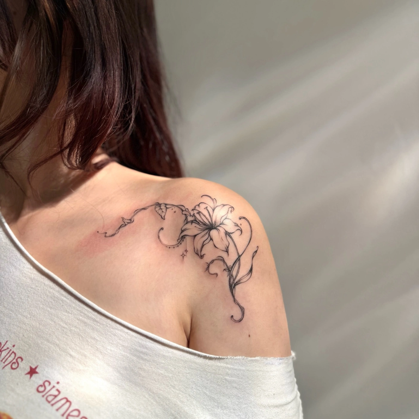 Fine-line floral tattoo of a lily on shoulder.